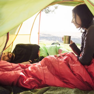 girl in red sleeping bag in green tent holding mug sleeping bags